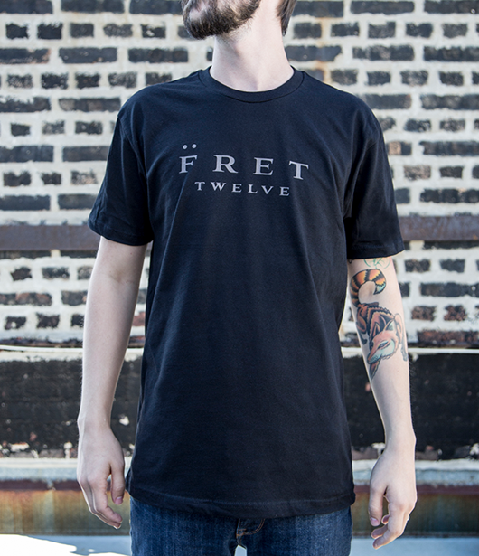 Model wearing black tee with spelled out Fret Twelve logo graphic.