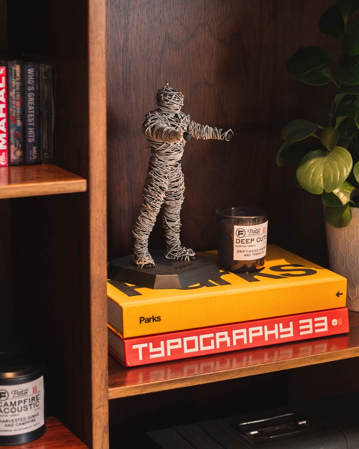 String Thing® guitar string upcycling mummy displayed as music room shelf art — fully wrapped with used guitar strings alongside FRET12 candle and design books and cassette tapes