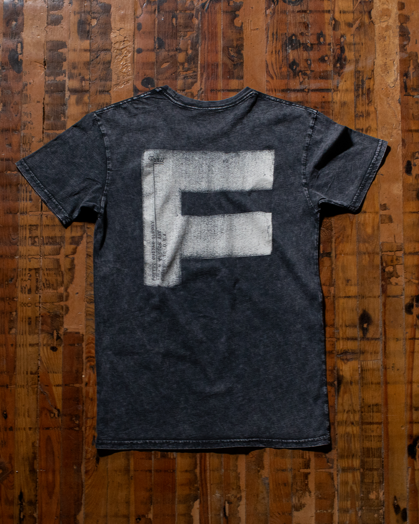 The black FAT F tee feels perfectly broken in. It features the FAT F graphic on the back and an industrial marking on the chest. 